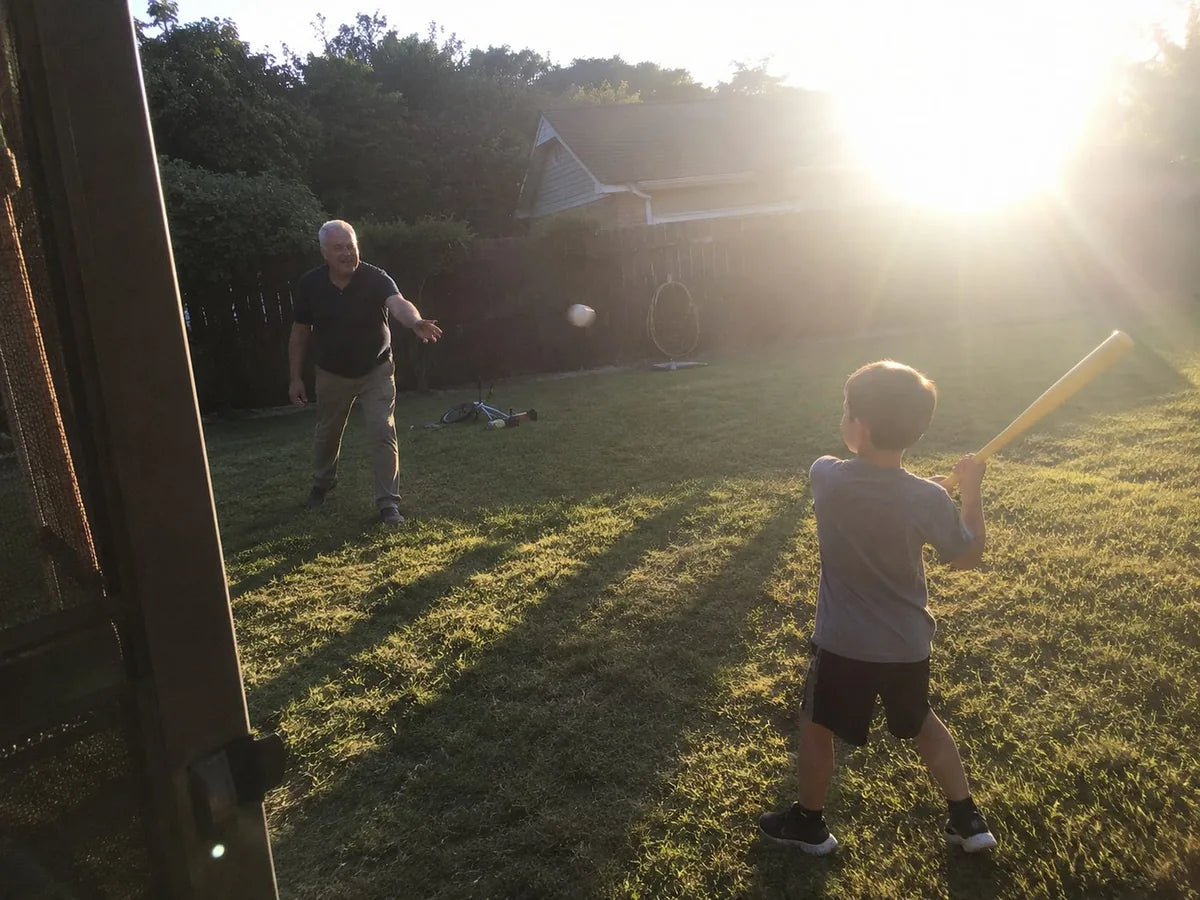 Ray pitching a wiffle ball to his grandson in late afternoon light, week twelve